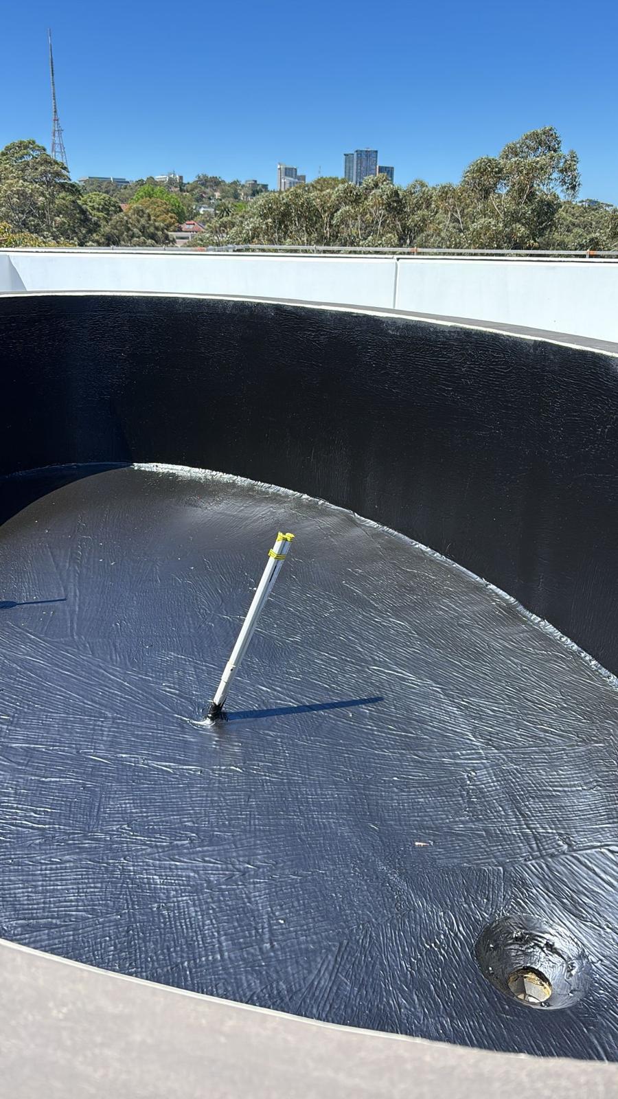 Curved concrete planter box lined in black membrane with a central pipe and corner drain