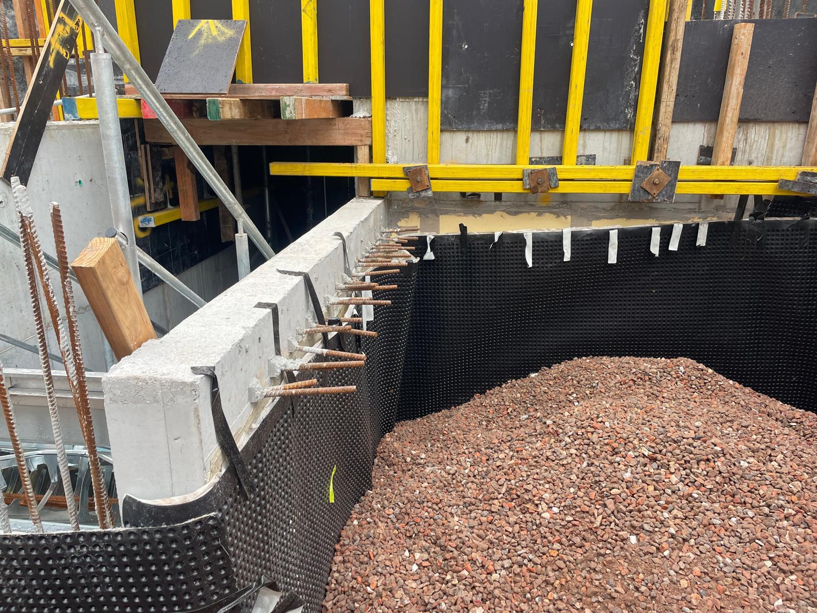 Black dimpled drainage membrane fixed to a concrete retaining wall with crushed stone backfill