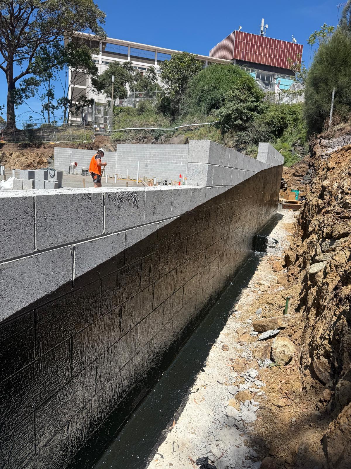 Long straight block retaining wall treated with black liquid membrane along the base courses
