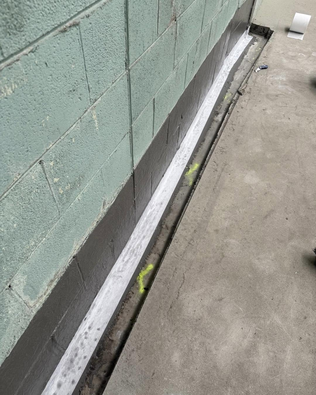 Block retaining wall base sealed with negative side waterproofing coating