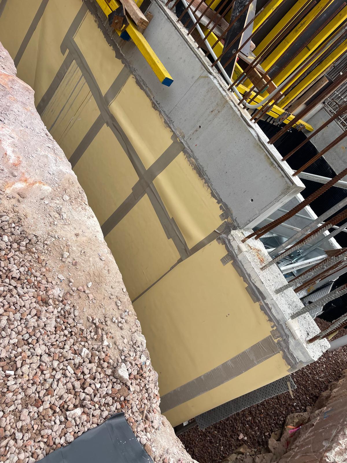 Yellow sheet waterproofing membrane with grey taped seams covering a concrete wall in an excavation