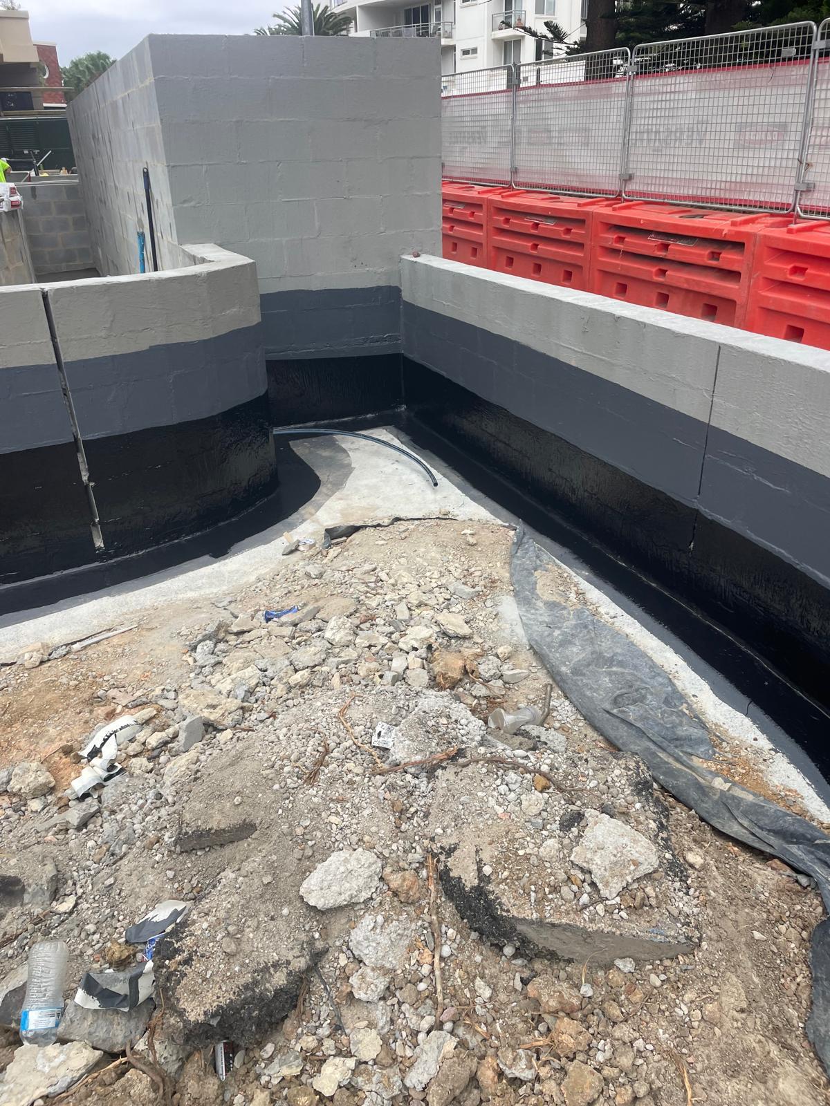 L-shaped block wall with black liquid membrane at the base and a dark grey band above