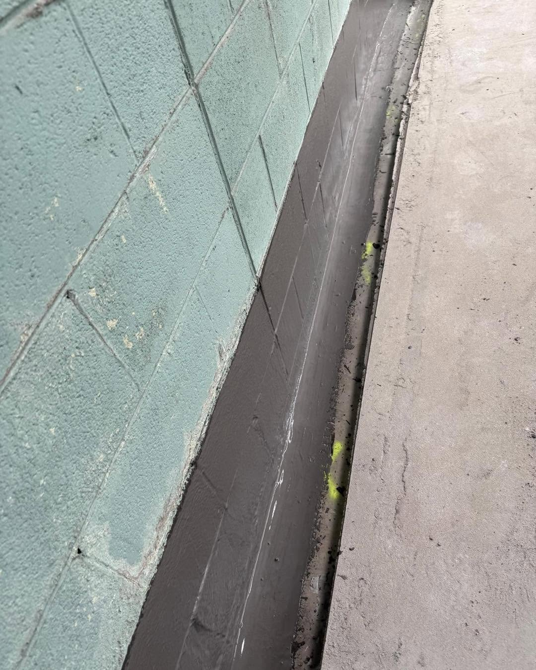 Wall-to-slab junction sealed with waterproofing membrane along a retaining wall