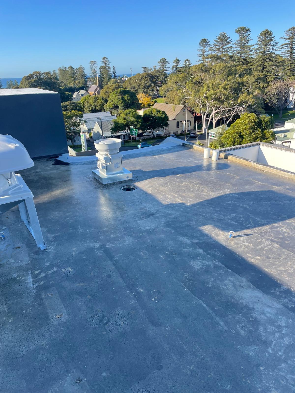 Concrete roof deck coated in grey waterproofing membrane around plant and vents