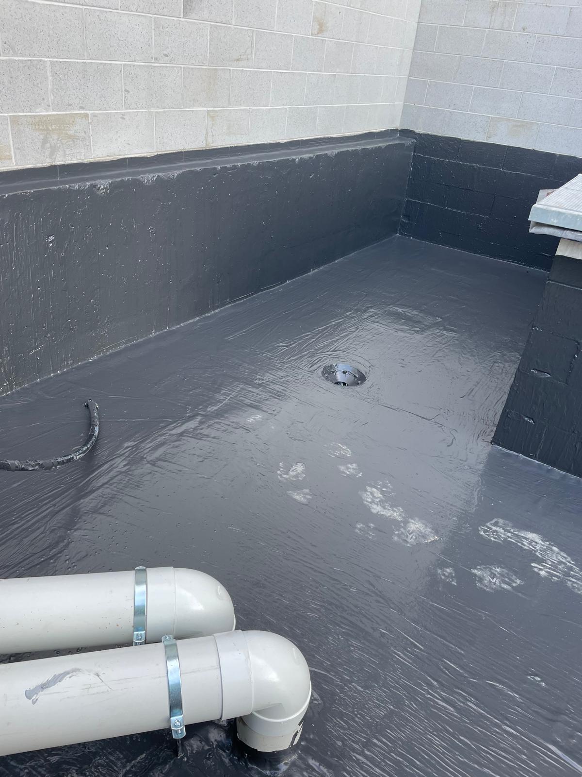 Masonry planter box corner coated in dark grey membrane with a floor drain and white PVC pipes