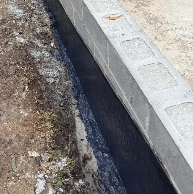 Black bituminous membrane coating the buried face of a block retaining wall along a narrow trench