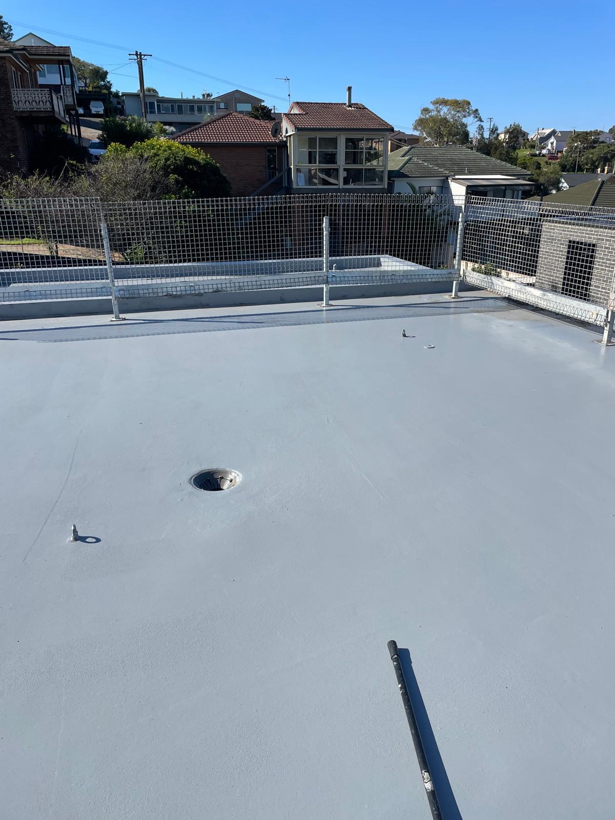 Roof slab coated in grey membrane with sealed floor waste and parapet edges