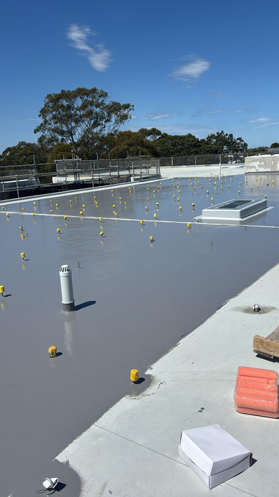 Large roof slab coated in grey waterproofing membrane around fixings and vents