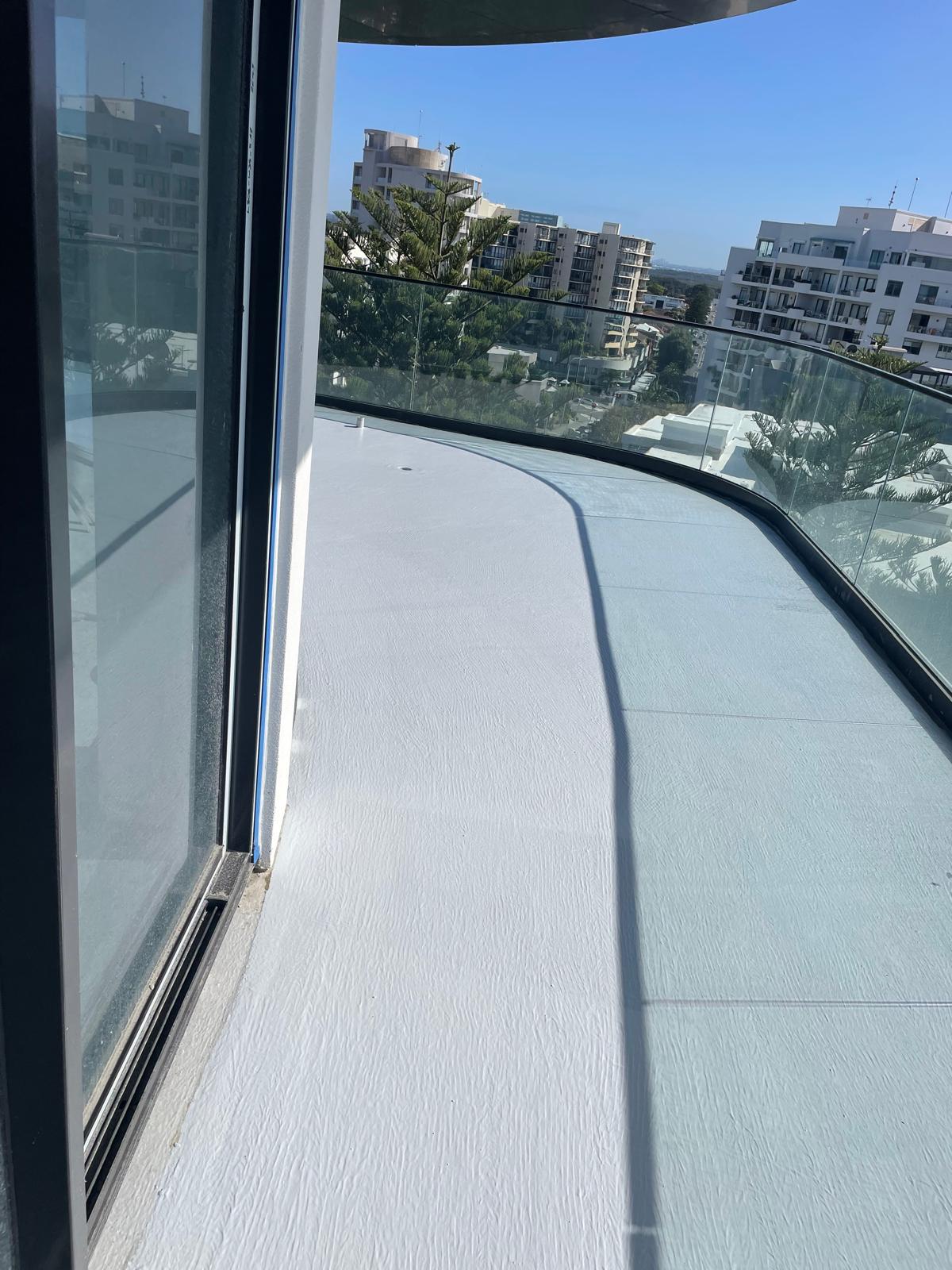 Curved high-rise balcony deck finished in white waterproofing membrane beside glass balustrade