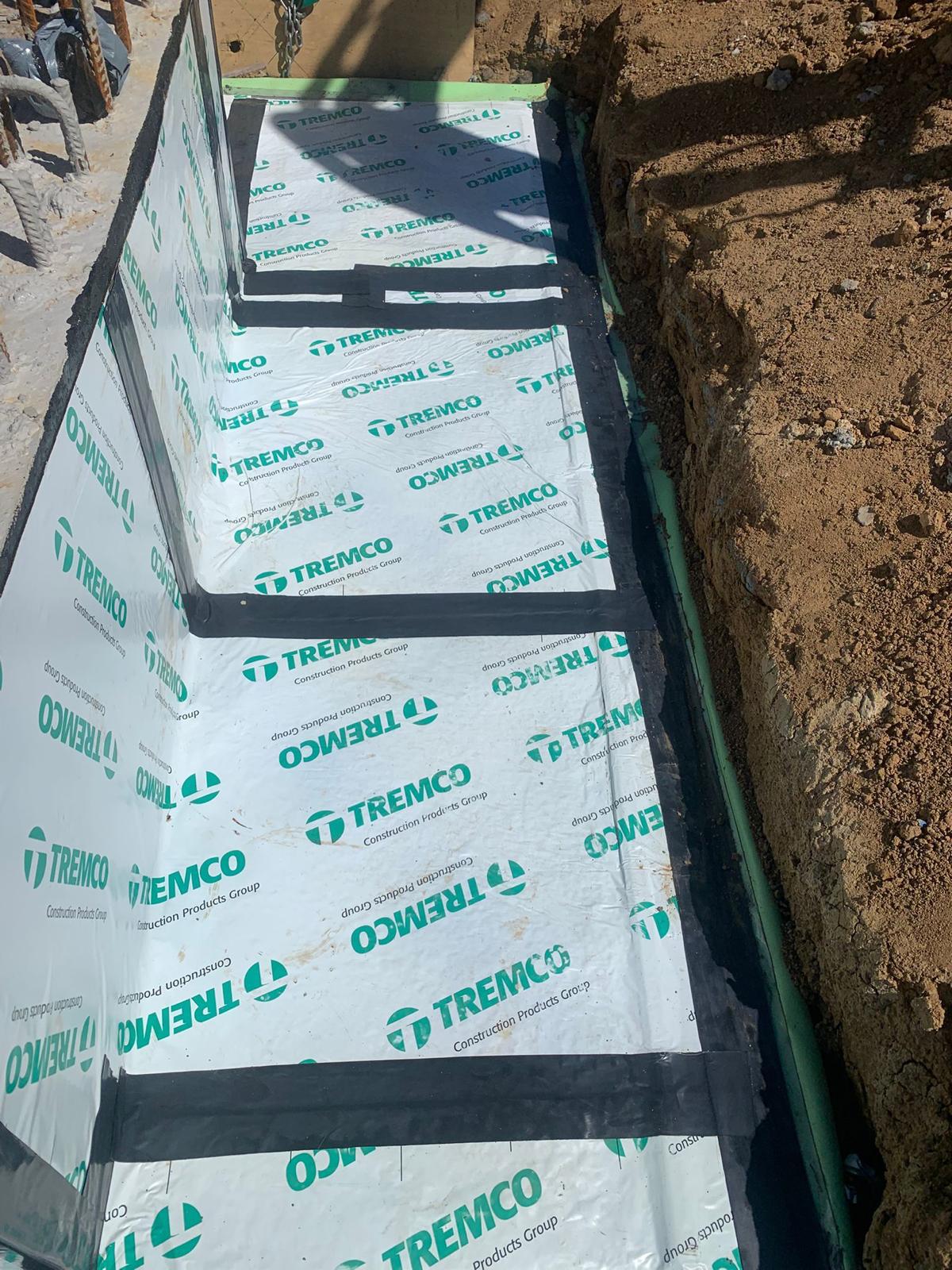 Tanking membrane sheets lapped and taped along a below grade wall trench