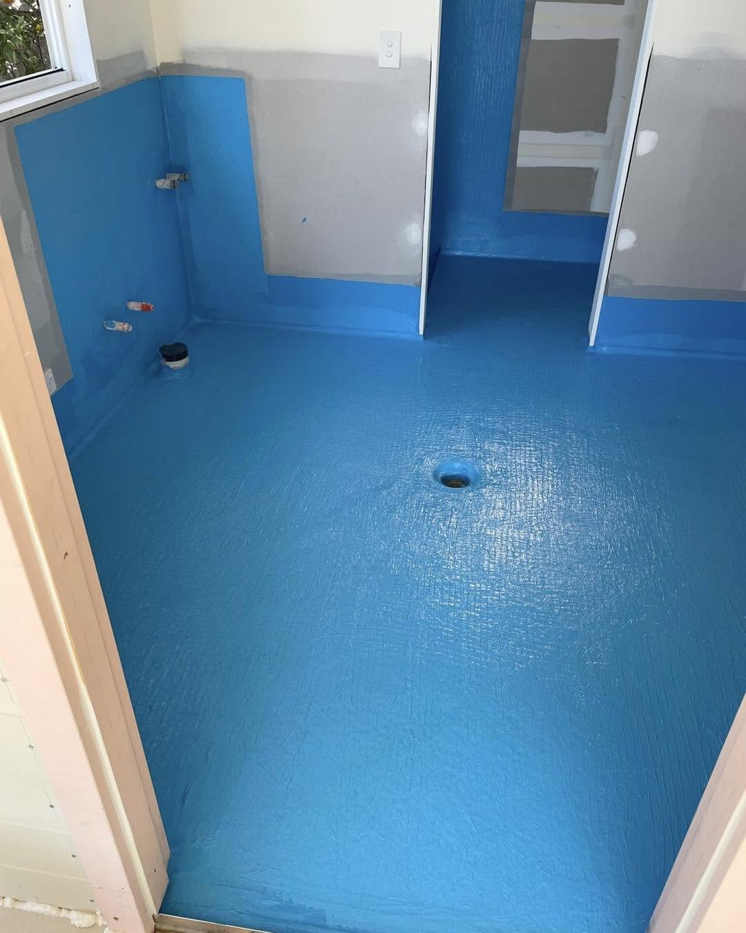 Bathroom floor and wall junctions coated in blue waterproofing membrane around the floor waste