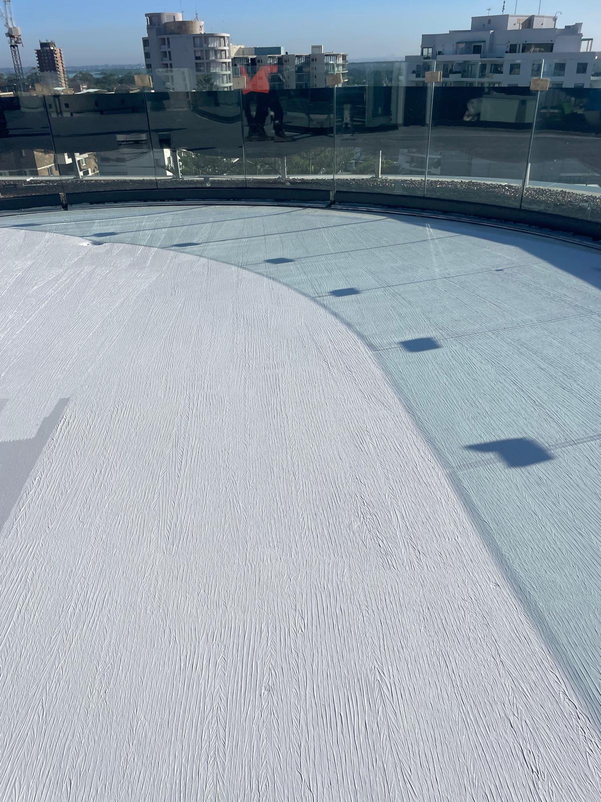 Curved rooftop terrace finished in white waterproofing membrane behind glass balustrade