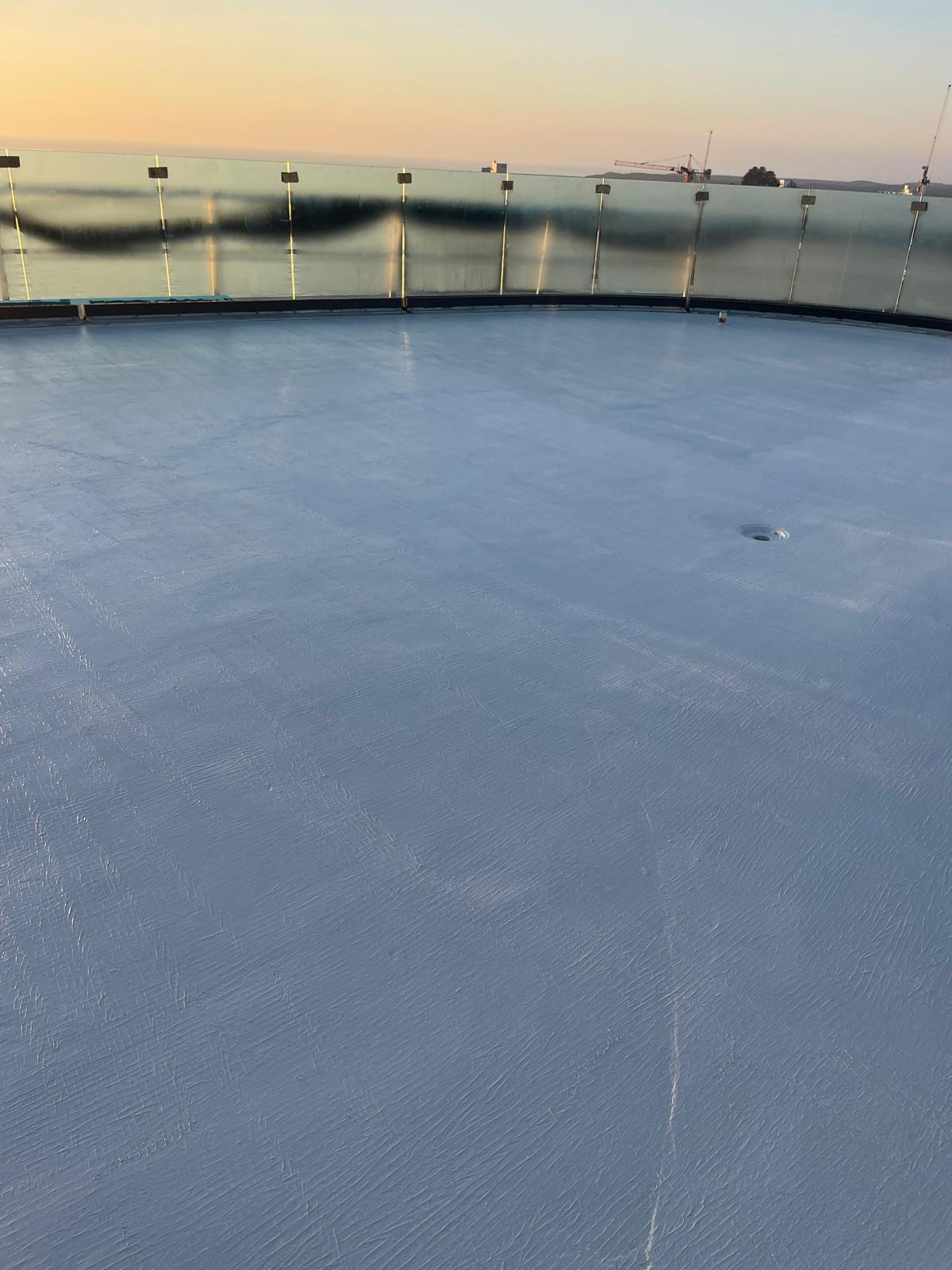 Curved rooftop terrace membrane at dusk behind a glass balustrade