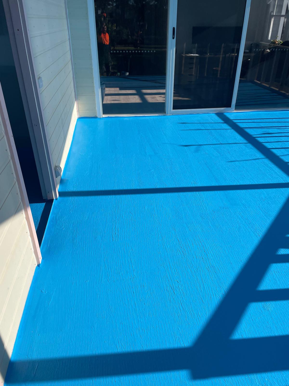 Balcony deck finished in bright blue waterproofing membrane beside sliding doors
