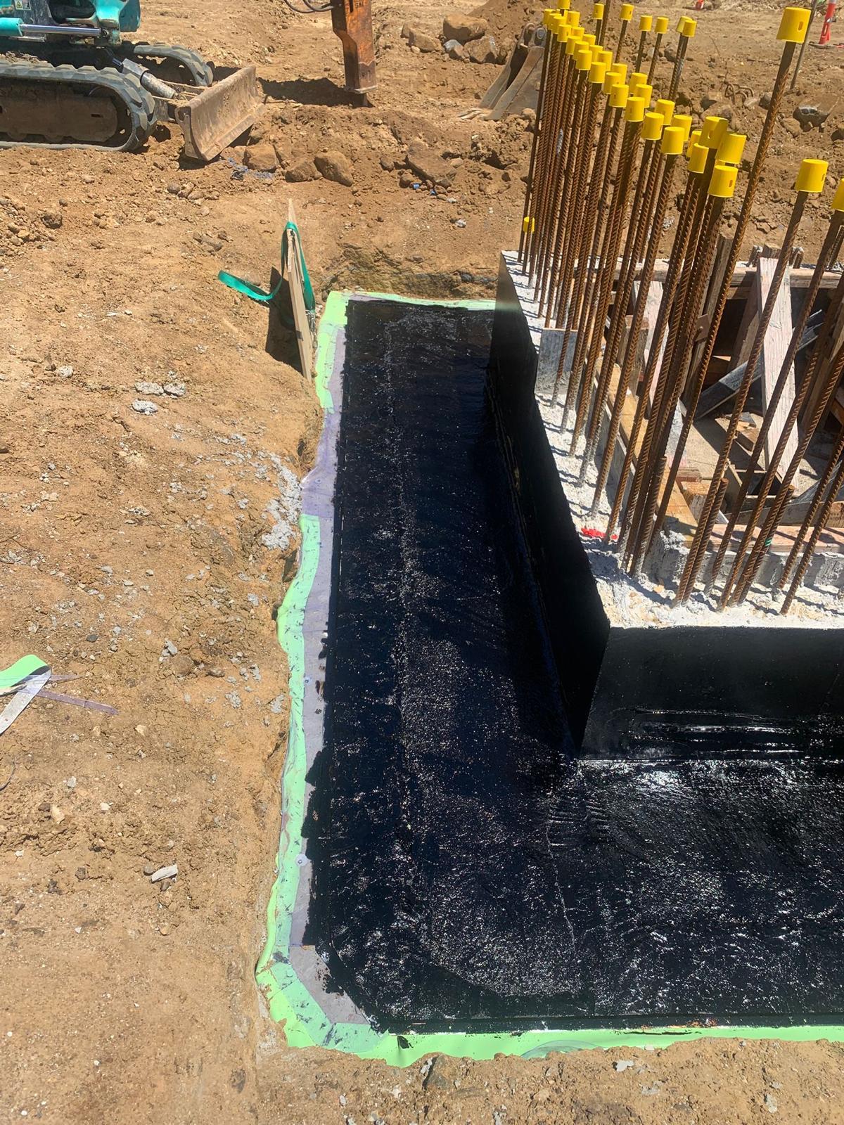 Below grade footing sealed with black bituminous tanking membrane before backfill
