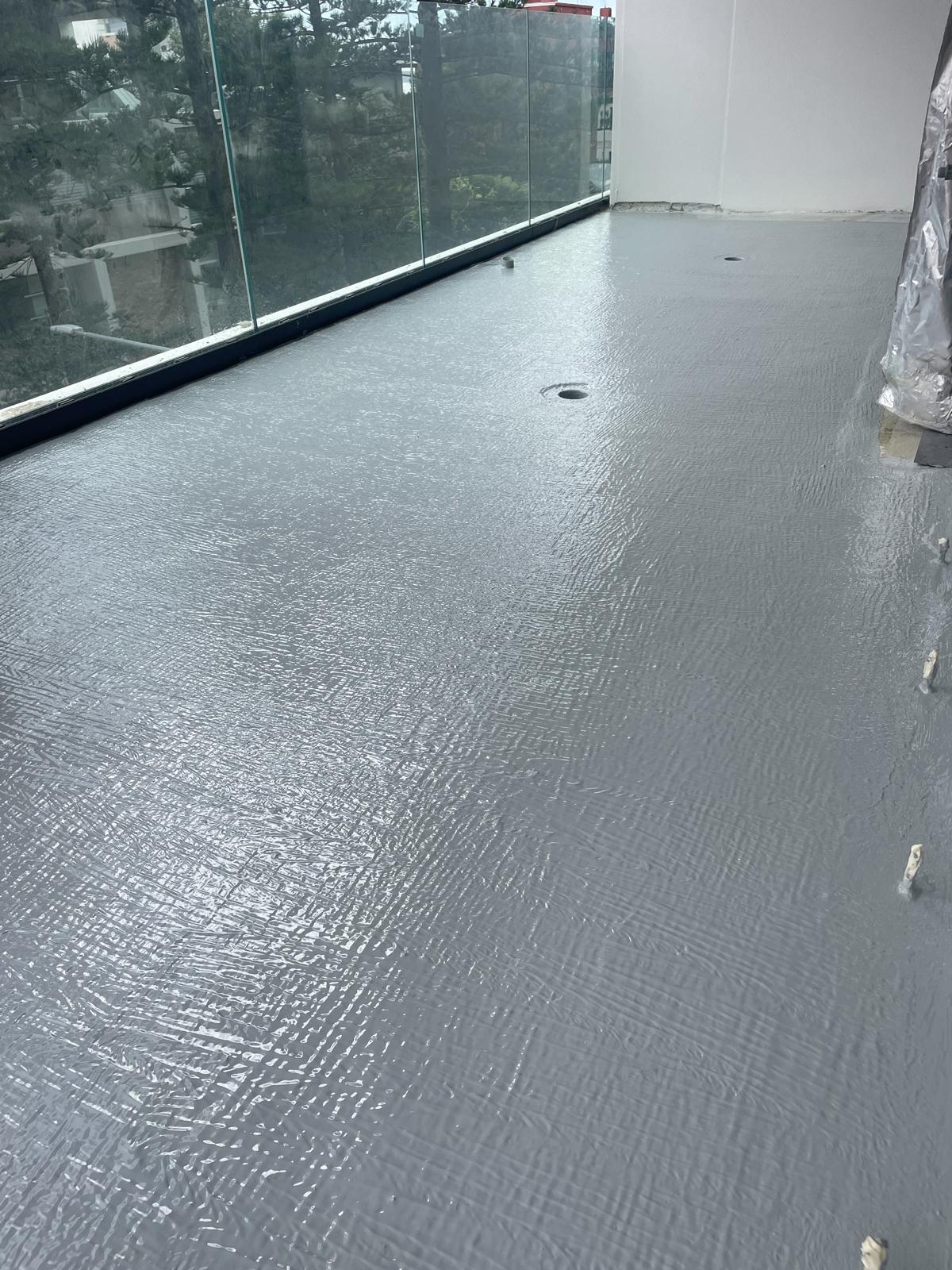 Wide balcony floor sealed with grey waterproofing membrane along the glass balustrade